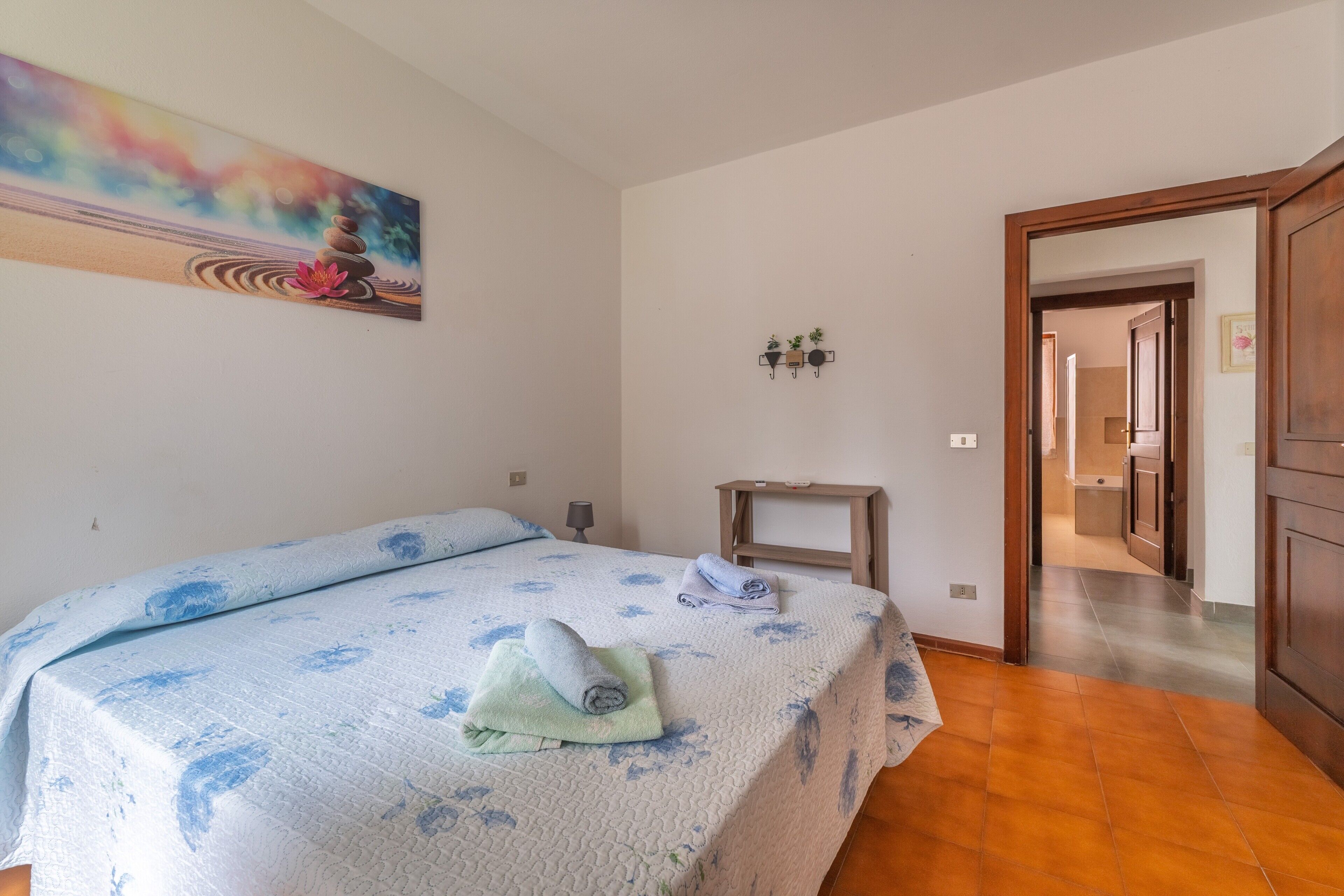 Un dormitorio con cama, un cuadro, una mesita de noche y un pasillo que conduce a otra habitación.