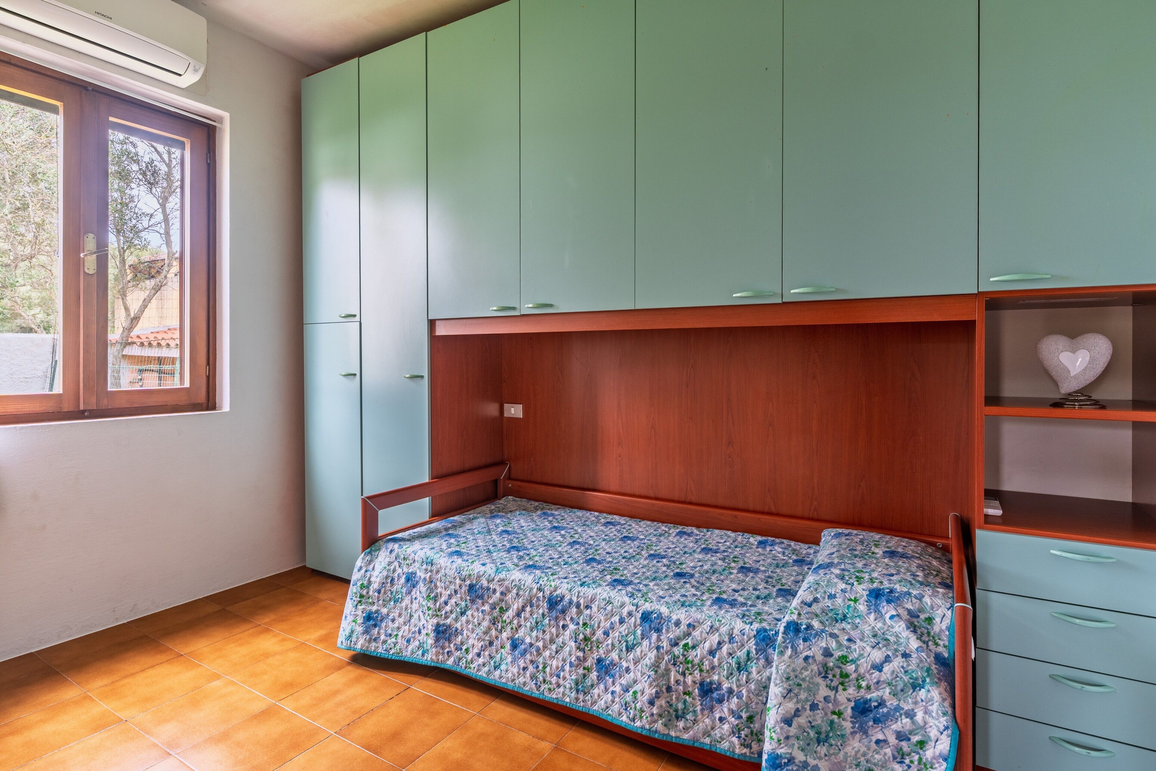 Ein Schlafzimmer mit einem Holzbett, grünen Schränken, einem Fenster und einem gefliesten Boden.