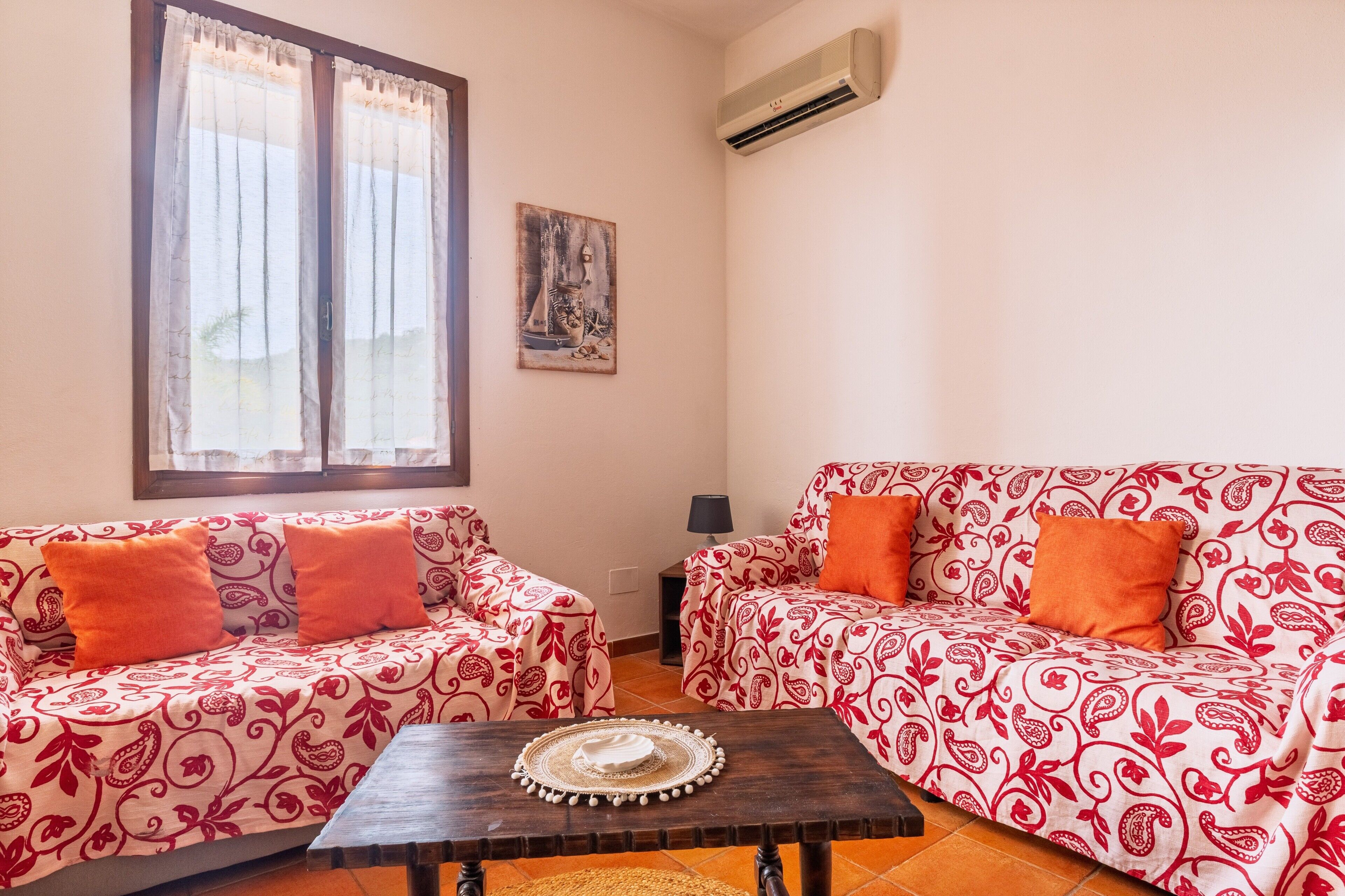A living room with two patterned sofas, a small table, and an air conditioning unit on the wall.