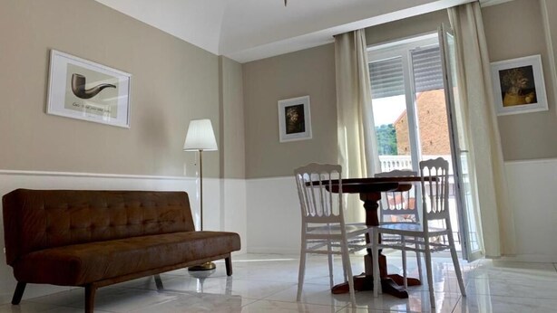 Una habitación con un sofá marrón, una mesa de comedor con sillas, un candelabro y cuadros en las paredes.