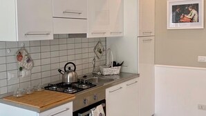 Una cocina con armarios blancos, estufa a gas, lavamanos y salpicadero de azulejos.