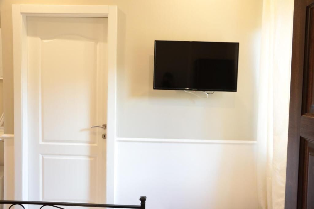 Una stanza con una porta bianca chiusa, un televisore a schermo piatto fissato al muro e una struttura letto in metallo.