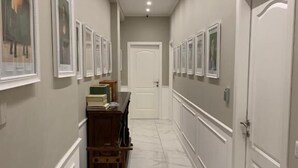 Un pasillo con cuadros en las paredes, un banco de madera y una puerta blanca al final.