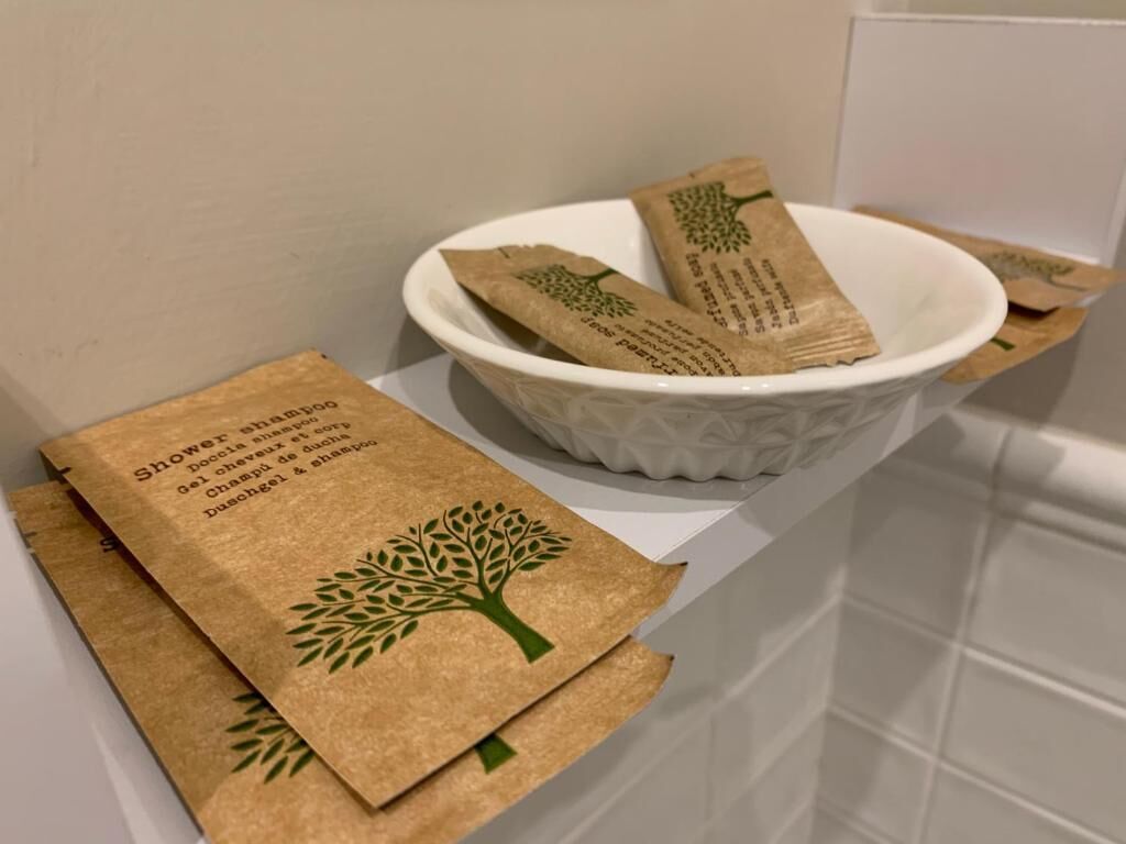 Un bagno con una bacinella bianca contenente asciugamani di carta marroni e un sacchetto di carta marrone con un motivo a tema alberi.