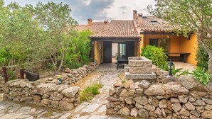 Un sentiero in pietra conduce a una casa con tetto in tegole, immersa nel verde e circondata da mura in pietra.