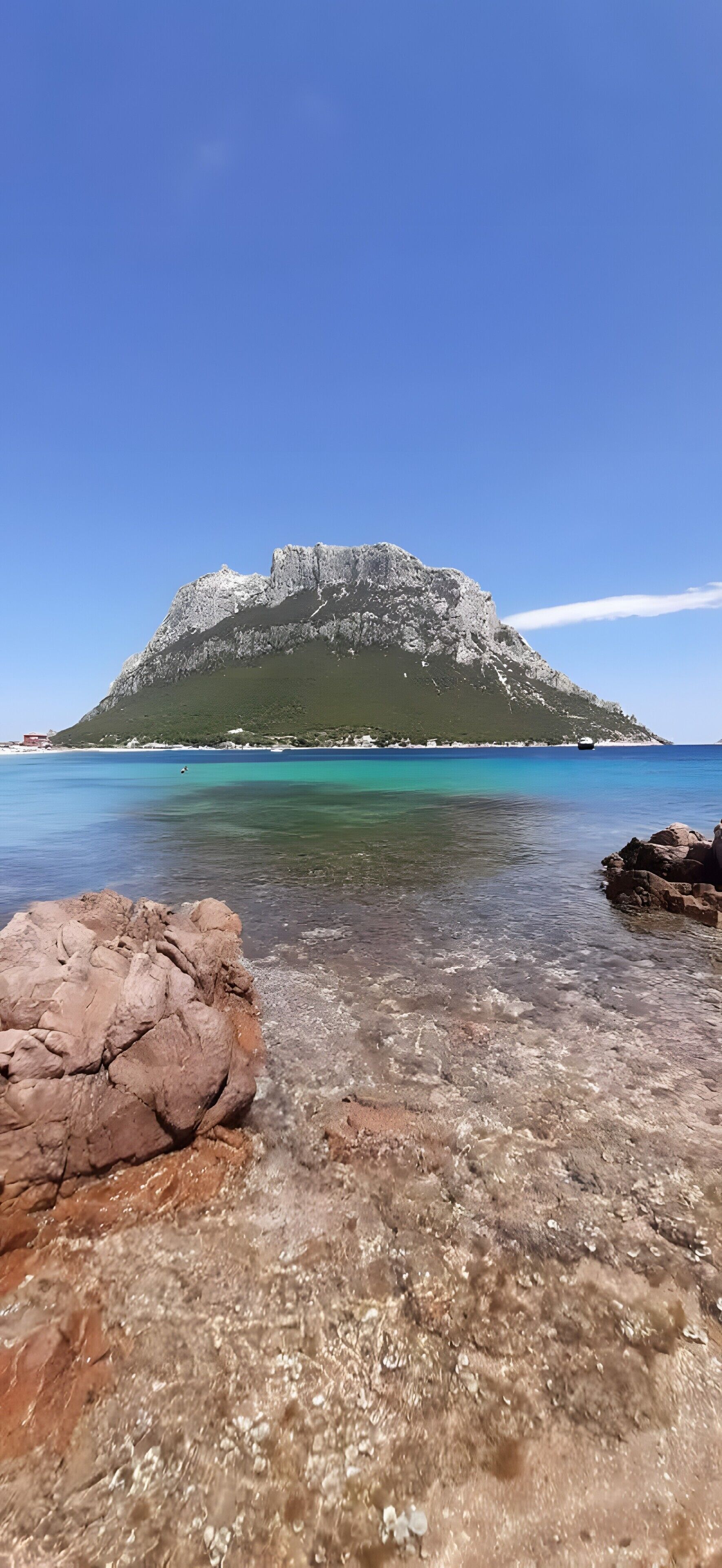 Eine felsige Küstenlinie mit klarem Wasser und einem Berg im Hintergrund.