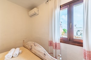Un dormitorio con cama, ventana con cortinas, equipo de aire acondicionado y vista al exterior.