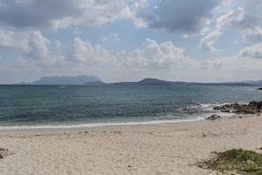 Una playa con arena, agua y montañas a lo lejos.
