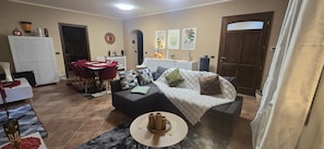 A living room with a sofa, a dining table, and chairs. There is a white cabinet and a door visible.