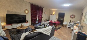 A living room with a TV, sofa, and dining area with chairs and a table.