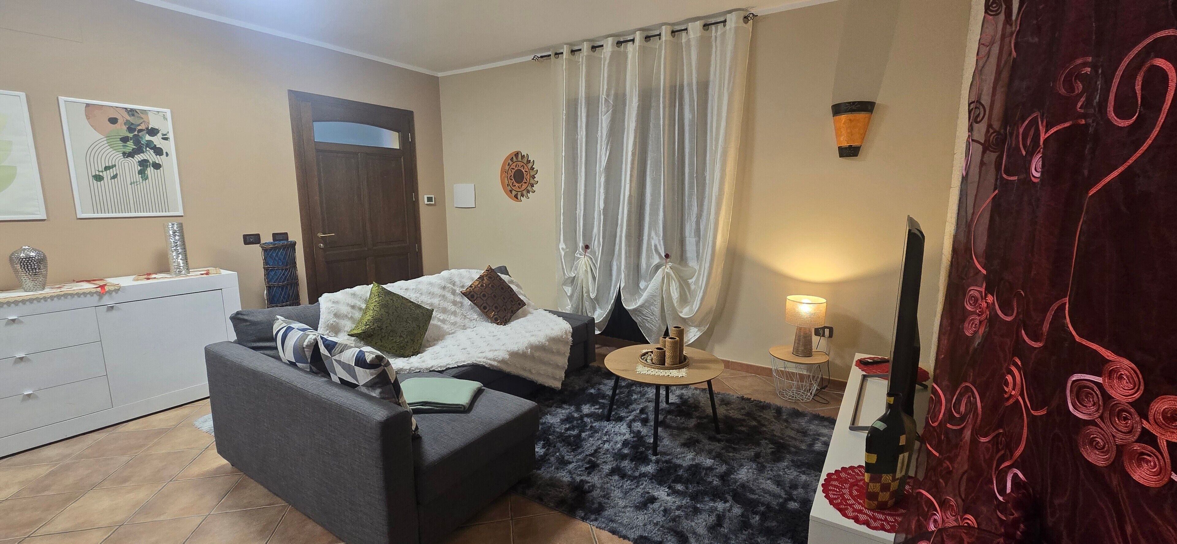 A room with a bed, a sofa, a small table, a lamp, a TV, and a door.