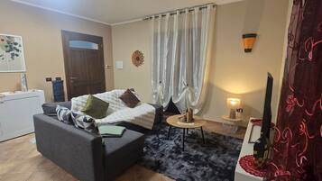 A room with a bed, a sofa, a small table, a lamp, a TV, and a door.