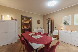A dining area with a table set for four, surrounded by red chairs, a white cabinet, and a kitchen in the background.