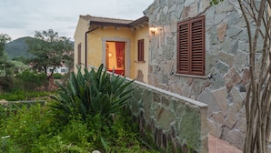 Un edificio de piedra con fachada amarilla, una puerta y un ventanal con contraventanas.