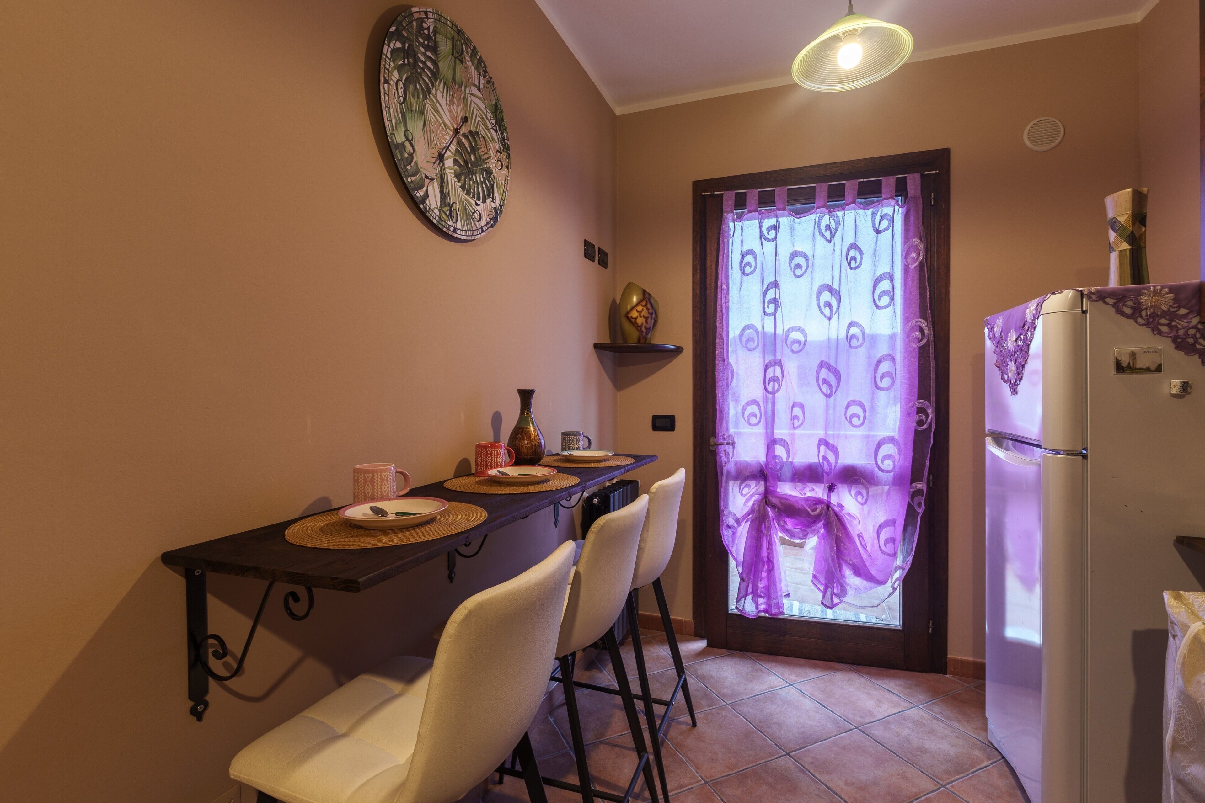Une petite cuisine comprenant une table à manger, des chaises, un réfrigérateur et un élément décoratif mural.