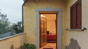 Una entrada de edificio con un arco de piedra, una planta en maceta, un felpudo rojo y un muro de piedra.