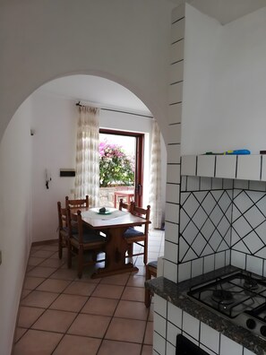 Una cocina con piso de baldosas, estufa a gas y comedor con mesa y sillas.