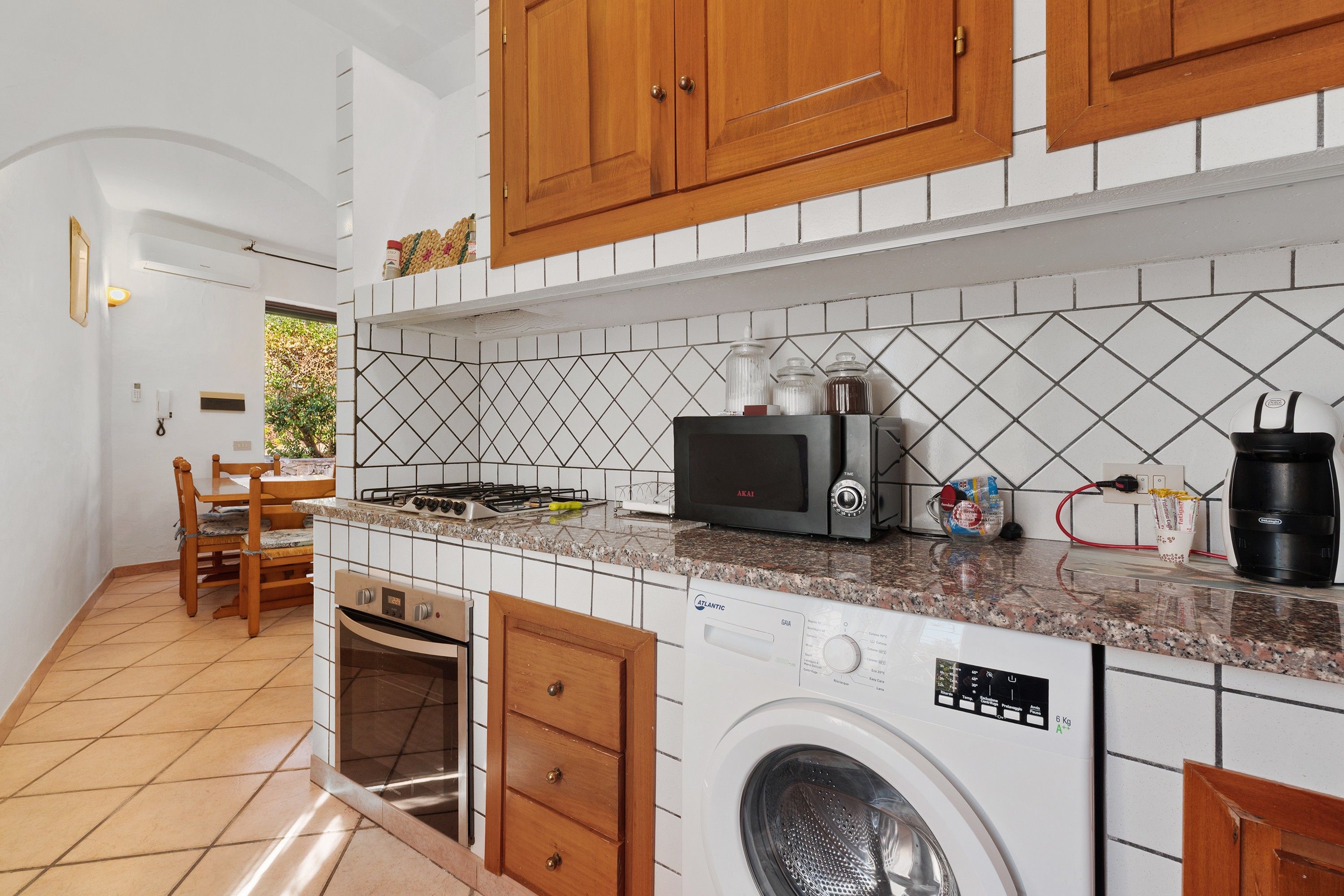 Una cocina compacta con horno integrado, microondas y lavadora, armarios de madera y salpicadero de azulejos.