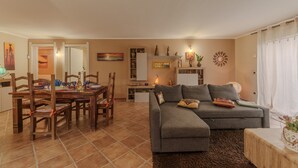 A living room with a sofa, a dining table with chairs, a kitchen area, and a hallway leading to another room.