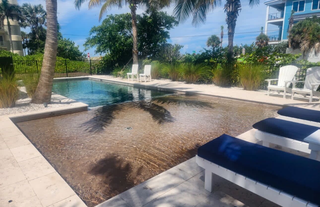 A swimming pool with clear water, surrounded by palm trees and white lounge chairs.