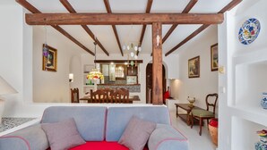 A living room with a grey sofa, red cushions, wooden beams, a dining area with chairs and a table, and a kitchen in the background. - Sea&Sun Premium Apartamento (Torrevieja)