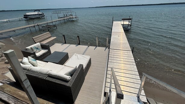 Een houten terras met lounge stoelen en een bank, uitkijkend over het water.