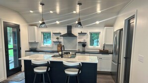 Een moderne keuken met een centraal eiland, twee barkrukken, hanglampen en een roestvrijstalen koelkast.