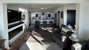 Een moderne keuken met een centraal eiland, een eetgedeelte met barkrukken, een grote flatscreen-tv en een gezellige zithoek met een bank en stoelen.