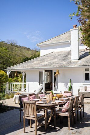 A patio area with a wooden table set for dining, surrounded by wicker chairs with cushions. - Palm Court, Polperro (Polperro, Looe)