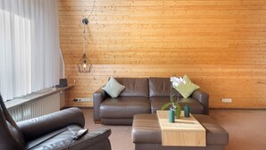 A modern living room with a brown leather sofa, a wooden coffee table, and a hanging light fixture.