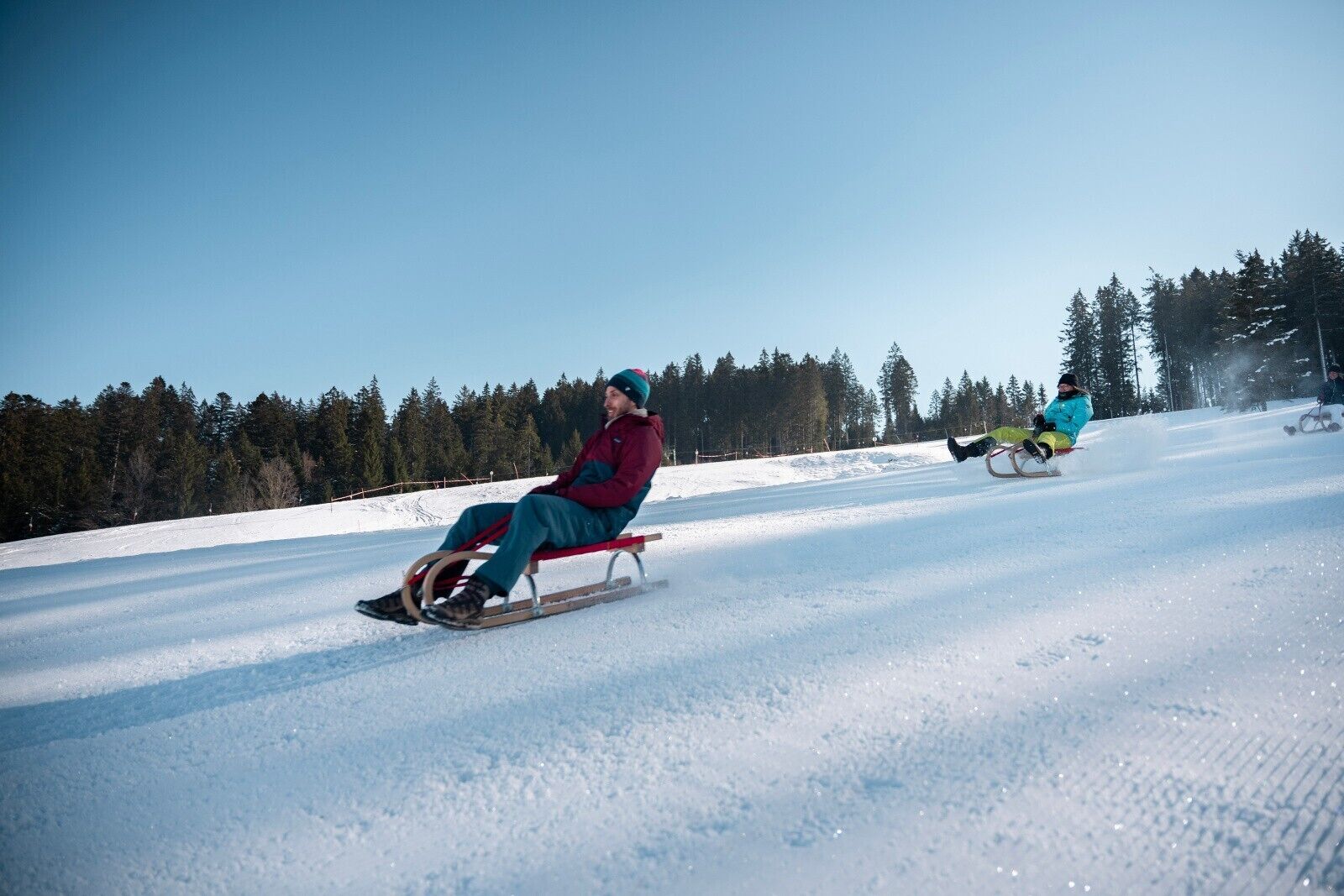 Un paysage enneigé avec une personne sur une luge et une autre personne en arrière-plan.