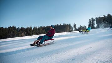 Un paysage enneigé avec une personne sur une luge et une autre personne en arrière-plan.