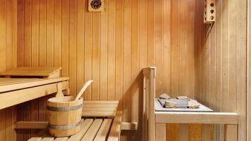 Ein Saunaraum mit Holzbänken, einem Holzeimer und einem Schöpfkellen sowie einer Sauna-Steuerung.