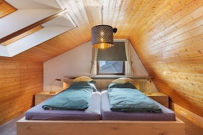Une chambre avec un plafond en pente, un puits de lumière, deux lits avec des oreillers assortis, des tables de chevet et un luminaire suspendu.