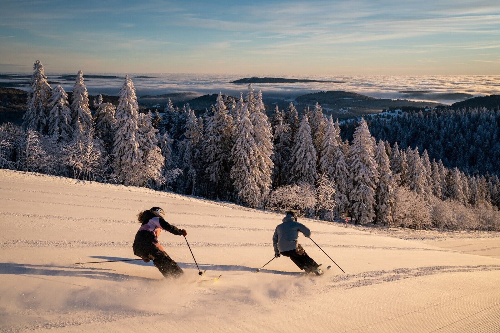 A snowy ski slope with skiers, snow-covered trees, and a clear sky.