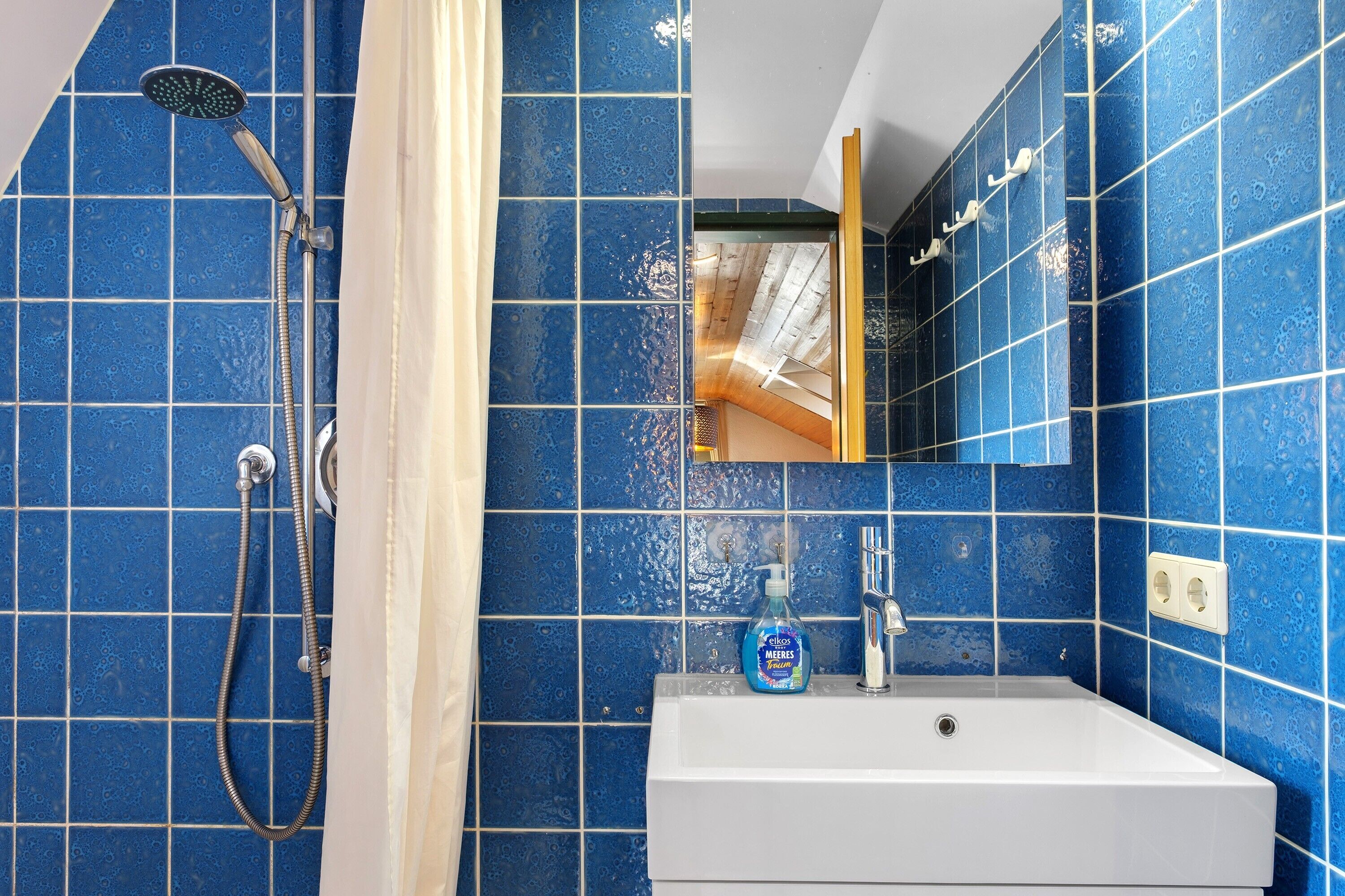 Een badkamer met blauwe tegels, een douche, een wastafel en een spiegel.