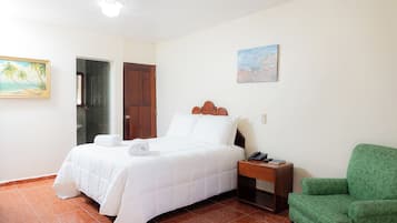 Una habitación de hotel con una cama, un sillón verde, un cuadro y una puerta de madera.