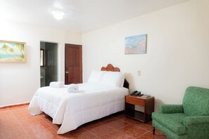 Een hotelkamer met een bed, een groene fauteuil, een schilderij en een houten deur.