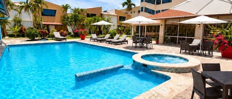 A swimming pool with lounge chairs and umbrellas, surrounded by buildings with large windows.