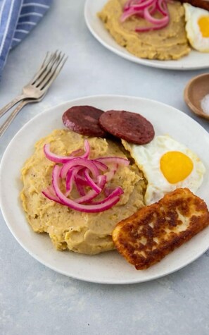 Un plato con una rebanada de pan, un huevo frito, una porción de salchicha y un poco de crema.