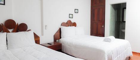 A hotel room with two beds, a wooden headboard, a nightstand, and a bathroom with a mirror and green tiles.