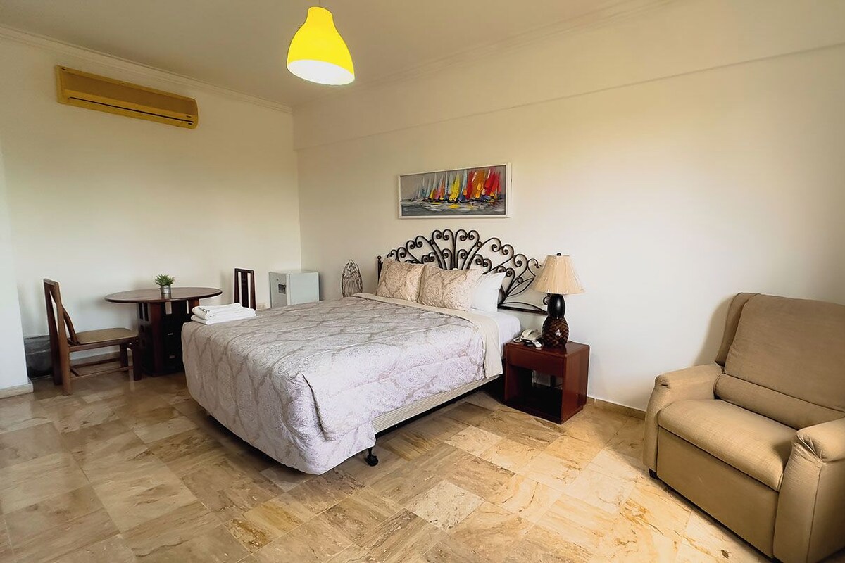 Un dormitorio con cama, una silla, una mesa y una lámpara.