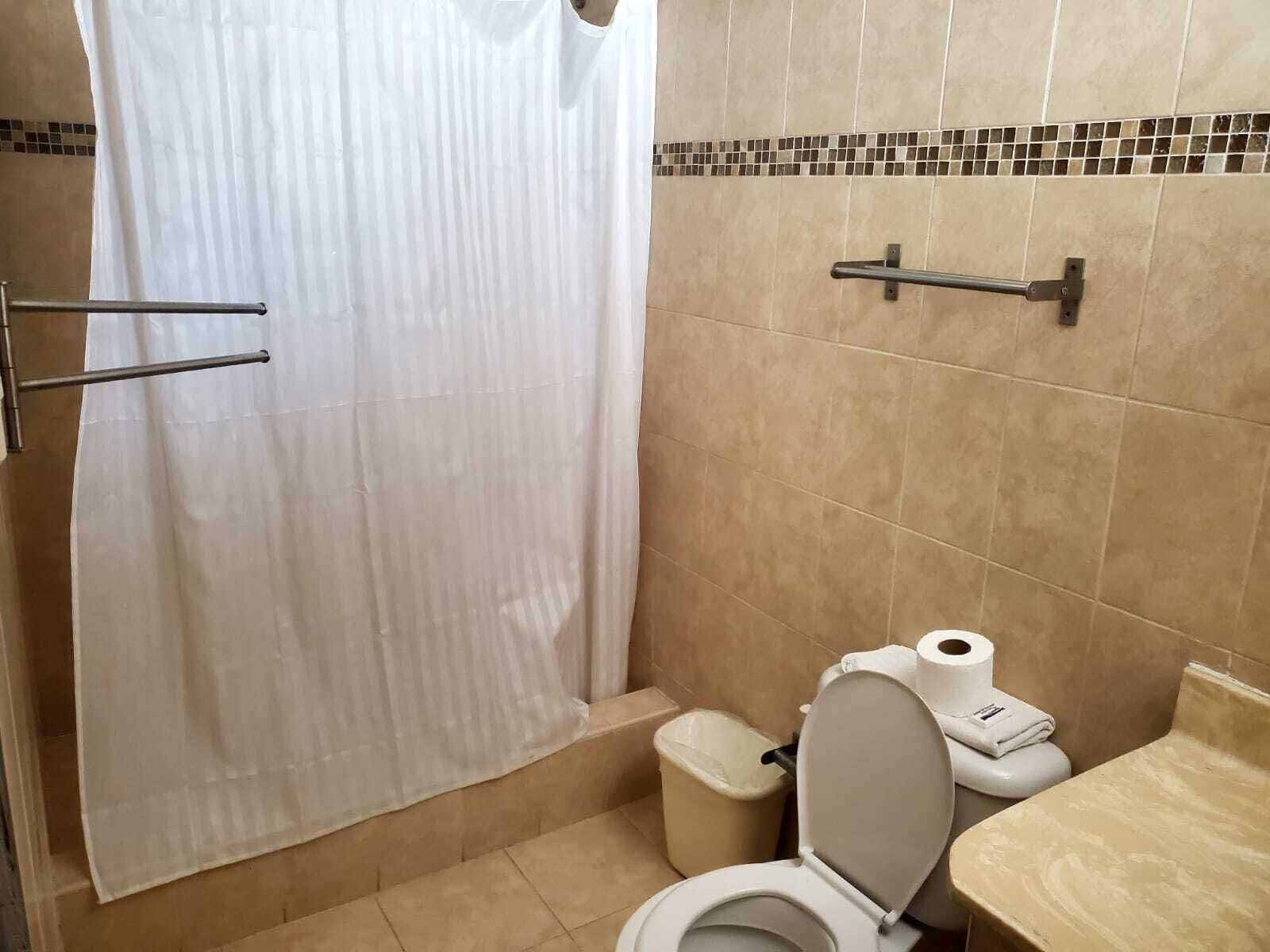 A bathroom with a shower curtain, a toilet, a trash bin, and a towel rack.