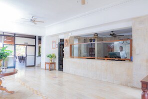 A hotel lobby with a reception desk, a ceiling fan, a large window, and a potted plant. - Hotel Tropicana (Santo Domingo Este)