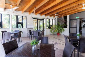 Un comedor interior con vigas de madera, mesas, sillas y plantas en macetas.