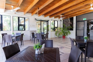 Un comedor interior con vigas de madera, mesas, sillas y plantas en macetas.