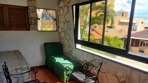 A balcony with a green sofa, two metal chairs, and a stone wall.