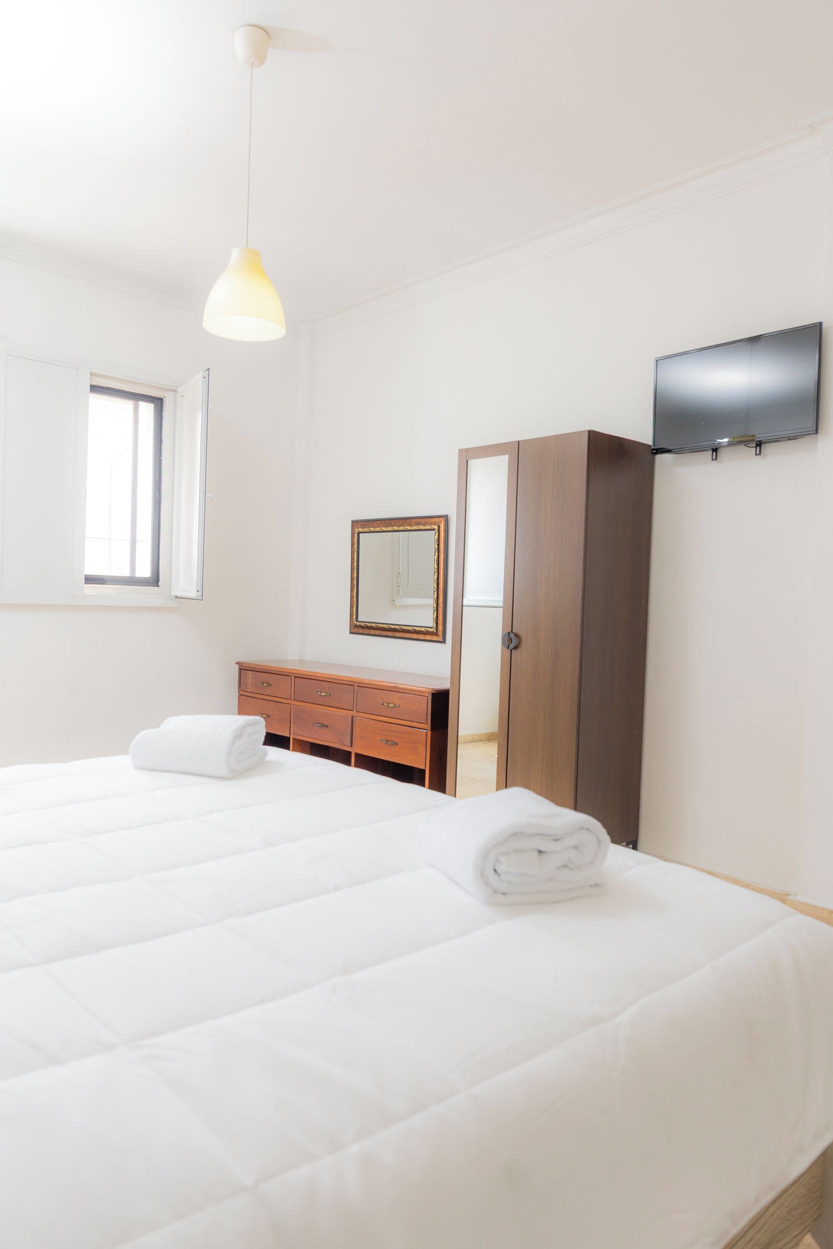 Habitación de hotel con cama, cómoda de madera, espejo, armario y televisión de pantalla plana en la pared.