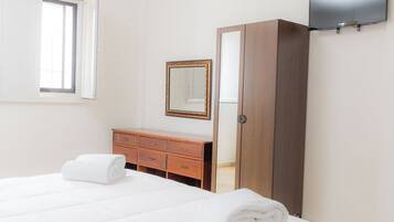Habitación de hotel con cama, cómoda de madera, espejo, armario y televisión de pantalla plana en la pared.
