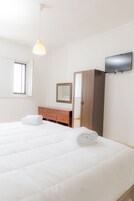 Habitación de hotel con cama, cómoda de madera, espejo, armario y televisión de pantalla plana en la pared.